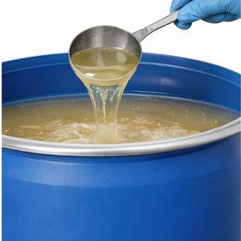 Gloved hand ladling pale yellow liquid from a blue industrial drum