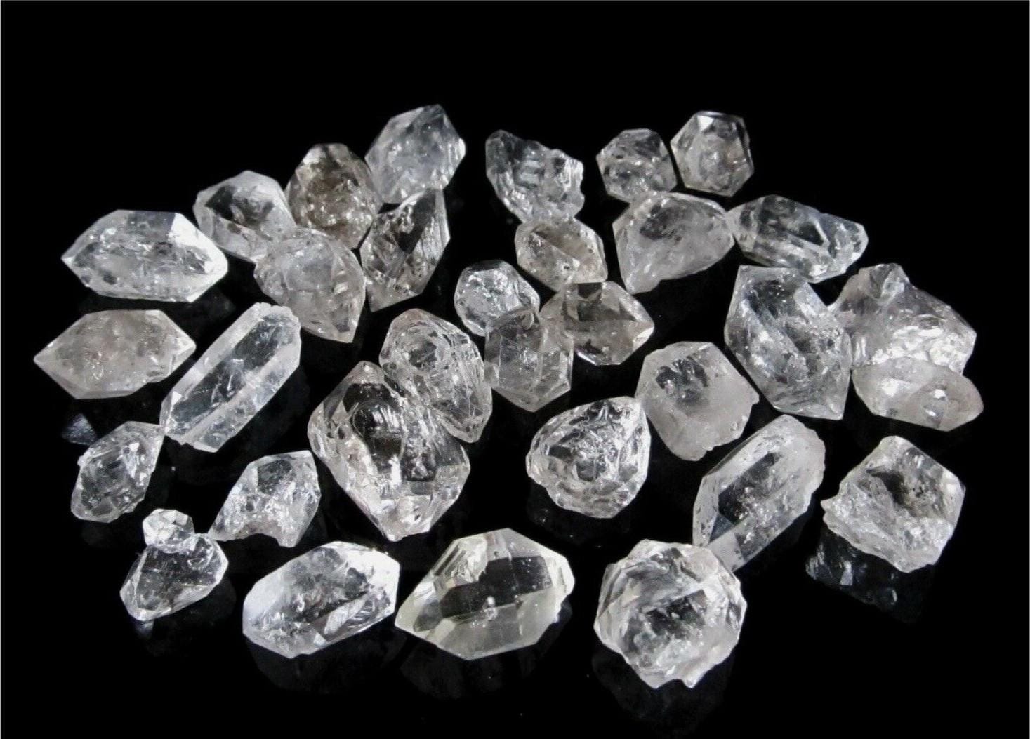 Heap of clear rough diamond crystals on a reflective black surface