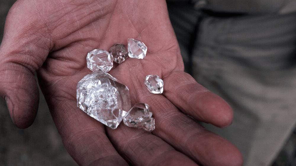 Several rough diamonds of mixed sizes held in an open weathered palm