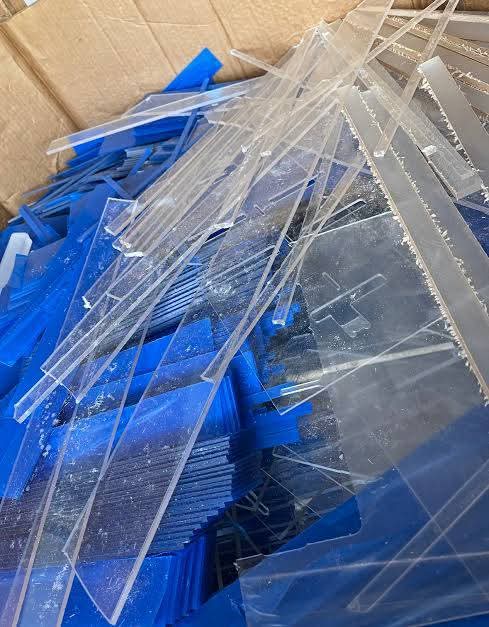 Clear and royal-blue acrylic strips with cutting dust in a cardboard box