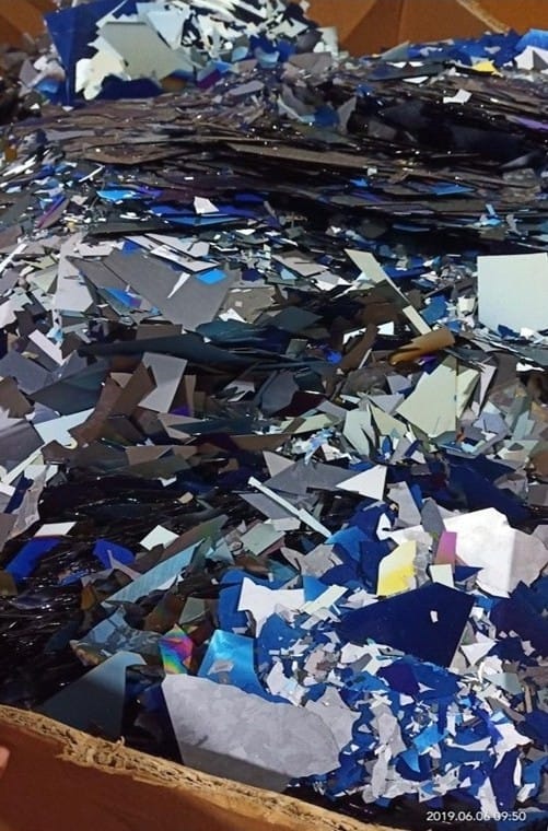 Dense pile of blue, silver, and iridescent thin scrap shards in a cardboard bin